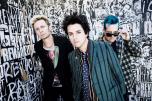 Members of the band Green Day standing by a graffiti-covered wall